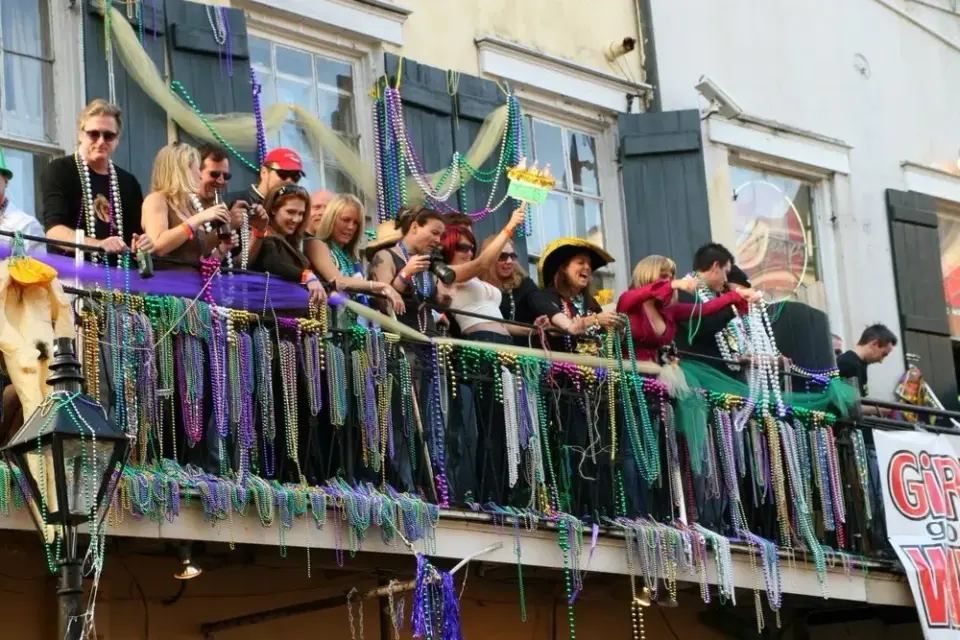 Revelers on a French Quarter balcony draped in strands of Mardi Gras beads