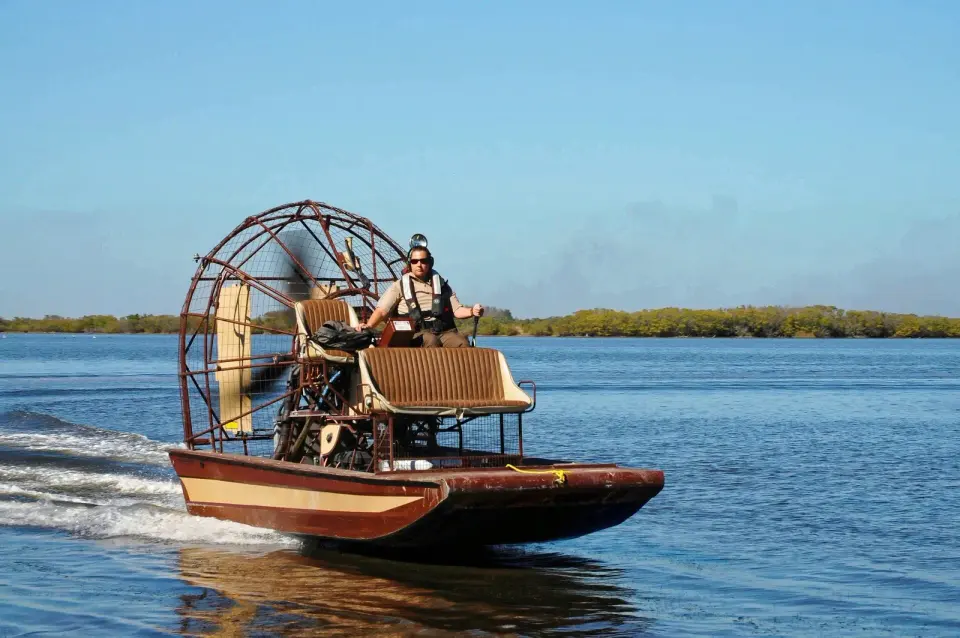 Captain steering an airboat with a large caged propeller across open water