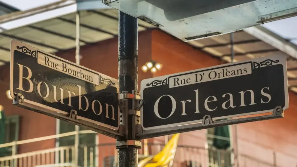 Crossed Bourbon and Orleans street signs above a French Quarter balcony in New Orleans