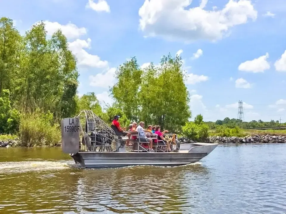 Airboat carrying seated passengers along a tree-lined Louisiana bayou under a bright summer sky