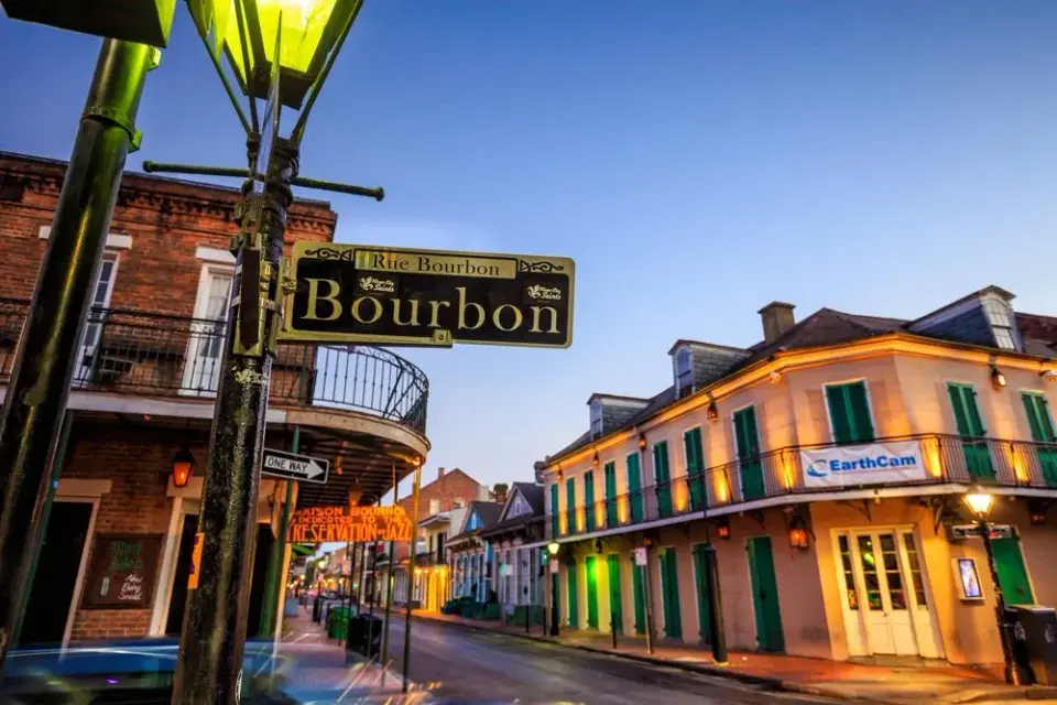 Illuminated Bourbon Street sign and gaslit balconies along the French Quarter at dusk