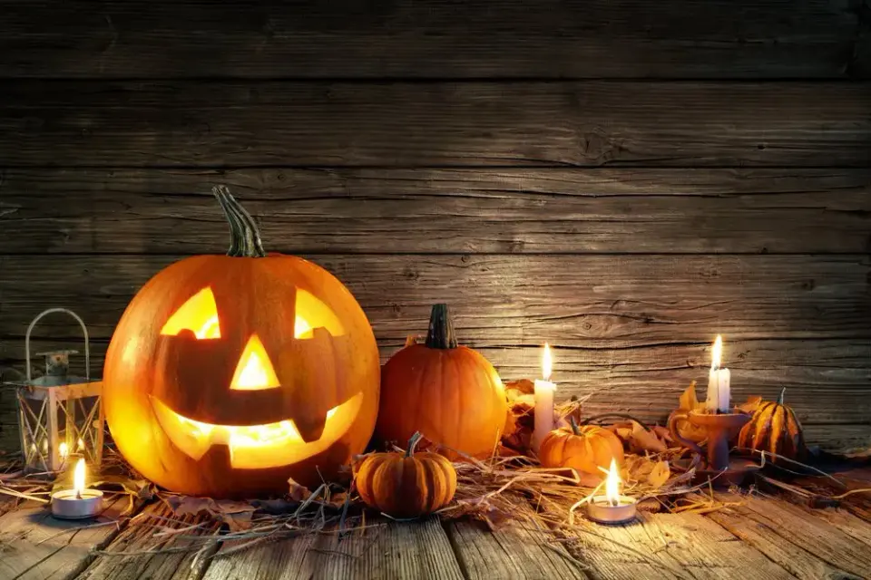 Glowing carved jack-o'-lantern surrounded by candles and small pumpkins on rustic wood