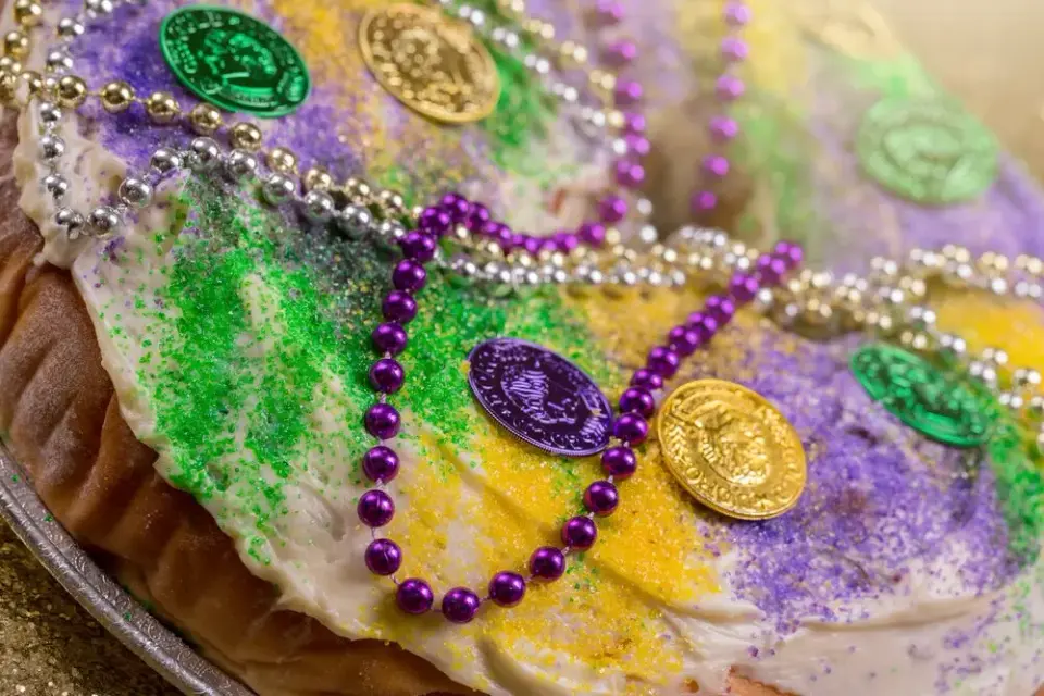 Close-up of frosted king cake topped with colored sugar, doubloons, and beaded necklaces