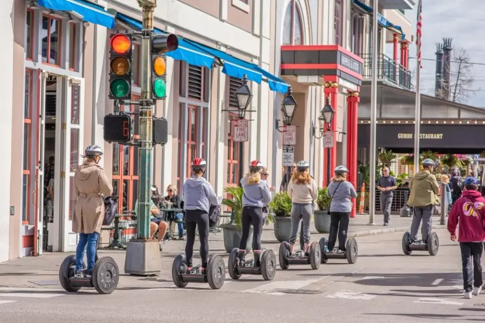 Helmeted tourists riding Segways past colorful storefronts on a sunny New Orleans street