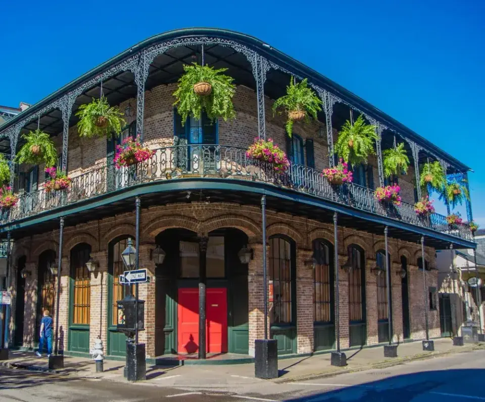 Historic French Quarter corner building with wrought-iron balconies, hanging ferns, and a red door