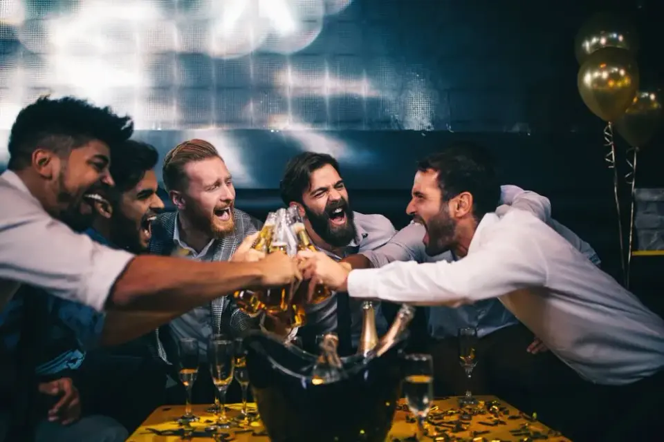 Group of men laughing and toasting beer bottles over a champagne bucket at a nightclub