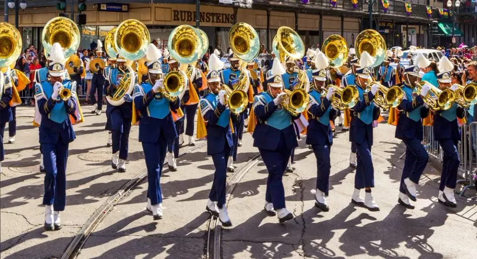 Marching band in blue and gold uniforms playing brass instruments during a New Orleans street parade