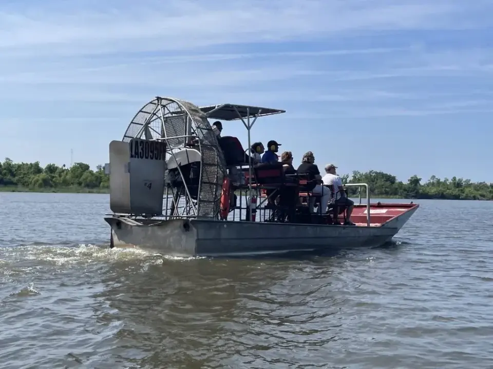 Passengers wearing ear protection aboard a canopied airboat crossing open bayou water