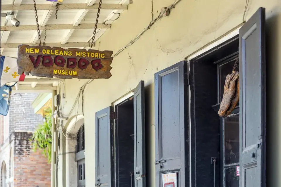 Weathered wooden sign for the New Orleans Historic Voodoo Museum outside a French Quarter storefront