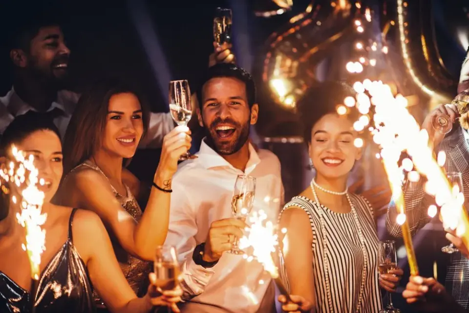 Smiling friends in formal wear toasting champagne with sparklers at a New Year's Eve party