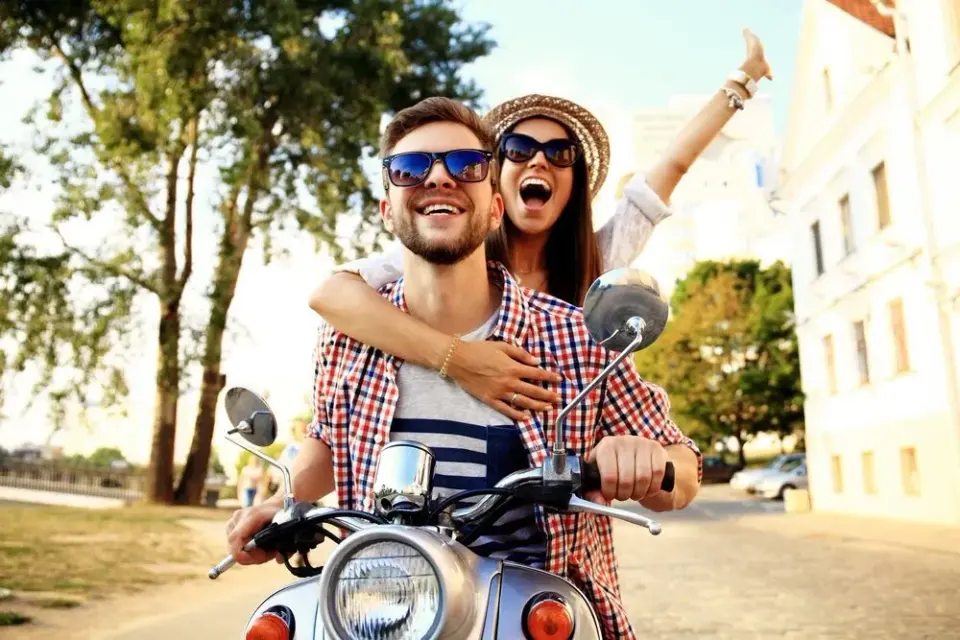 Laughing young couple riding a scooter together down a sunny tree-lined street