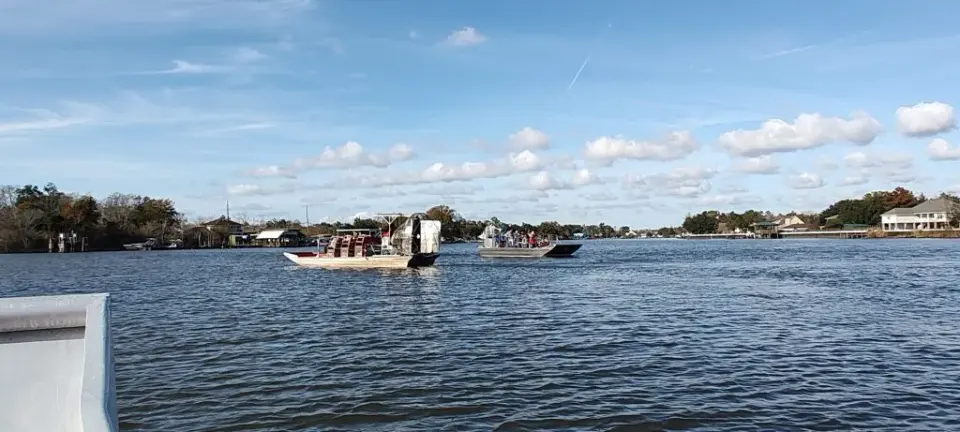 Two airboats carrying tour groups across a wide open waterway under a cloud-dotted sky