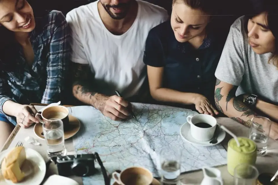 Four friends leaning over a road map with coffee cups while planning a trip
