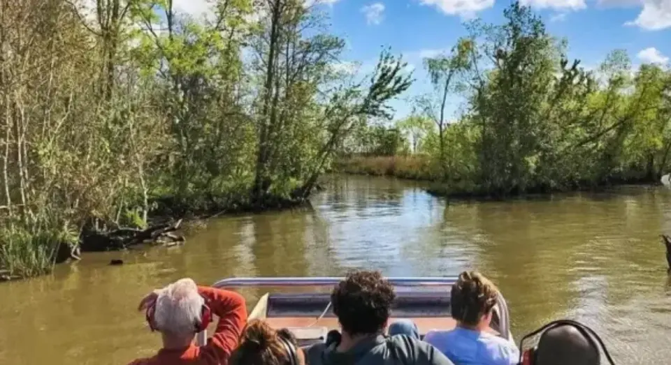 Passengers in casual clothes riding a tour boat down a tree-lined bayou channel