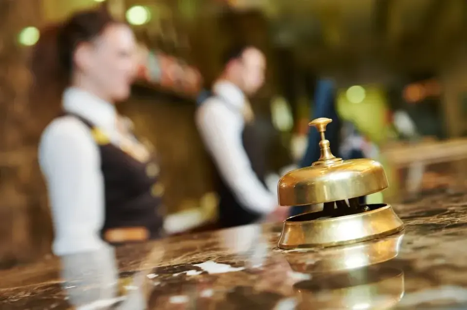 Brass service bell on a marble hotel front desk with staff greeting guests behind it