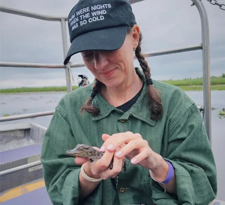 A New Orleans swamp tour guest gently cradles a tiny baby alligator in her hands aboard the boat, capturing the thrill of up-close wildlife encounters in the New Orleans swamp.