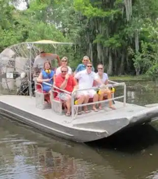A small airboat carrying a group of tourists glides through the Louisiana swamp, giving an intimate New Orleans airboat tour experience.
