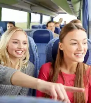 Two visitors smile and point out sights from inside a comfortable tour shuttle bus, illustrating the convenient round-trip pickup service for swamp tours from the New Orleans French Quarter.